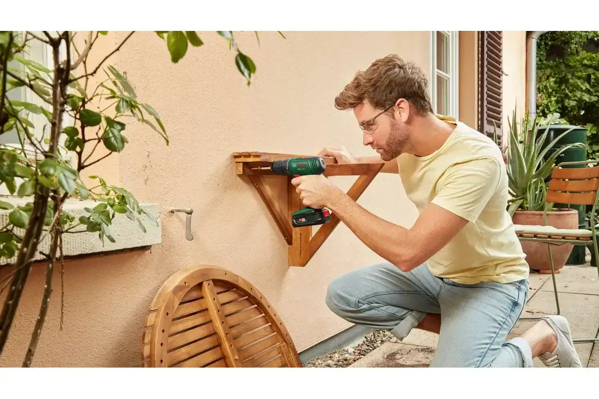 Man using cordless power drill to assemble wooden shelf outdoors on patio
