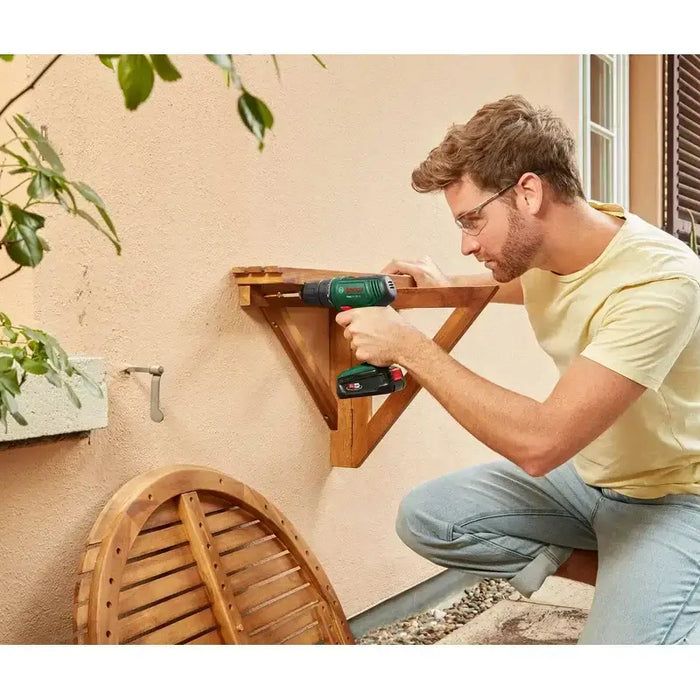 Man using cordless power drill to assemble wooden shelf outdoors on patio