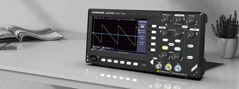 HANMATEK DOS1102S oscilloscope on a table showing waveform, essential tool for electronics enthusiasts.