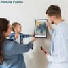 Family hanging a picture with stud finder frame on the wall while using a hammer, showcasing a bonding moment with a child.