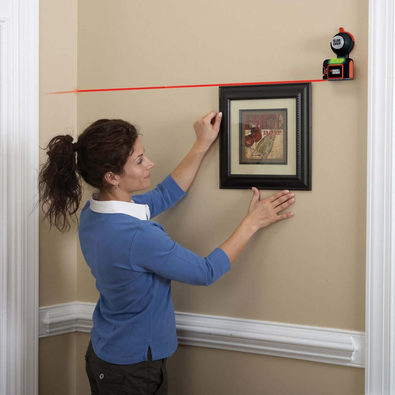 Family hanging a picture with stud finder frame on the wall while using a hammer, showcasing a bonding moment with a child.