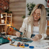 Woman using welding equipment for professionals at a workbench with tools and circuit boards