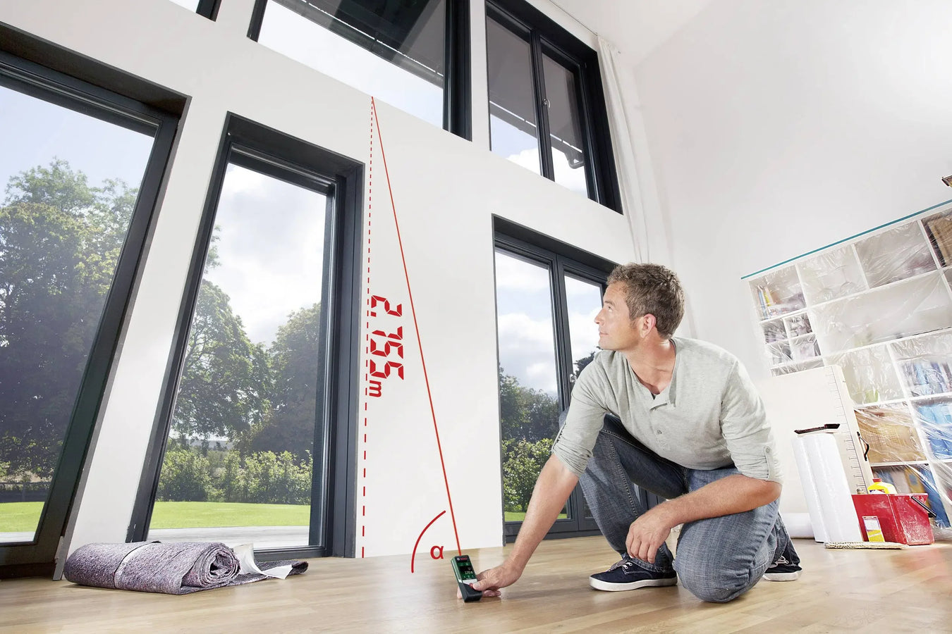 Person using a laser distance meter to measure height in a well-lit indoor space with large windows