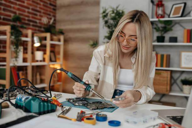 Woman using welding equipment for professionals at a workbench with tools and circuit boards