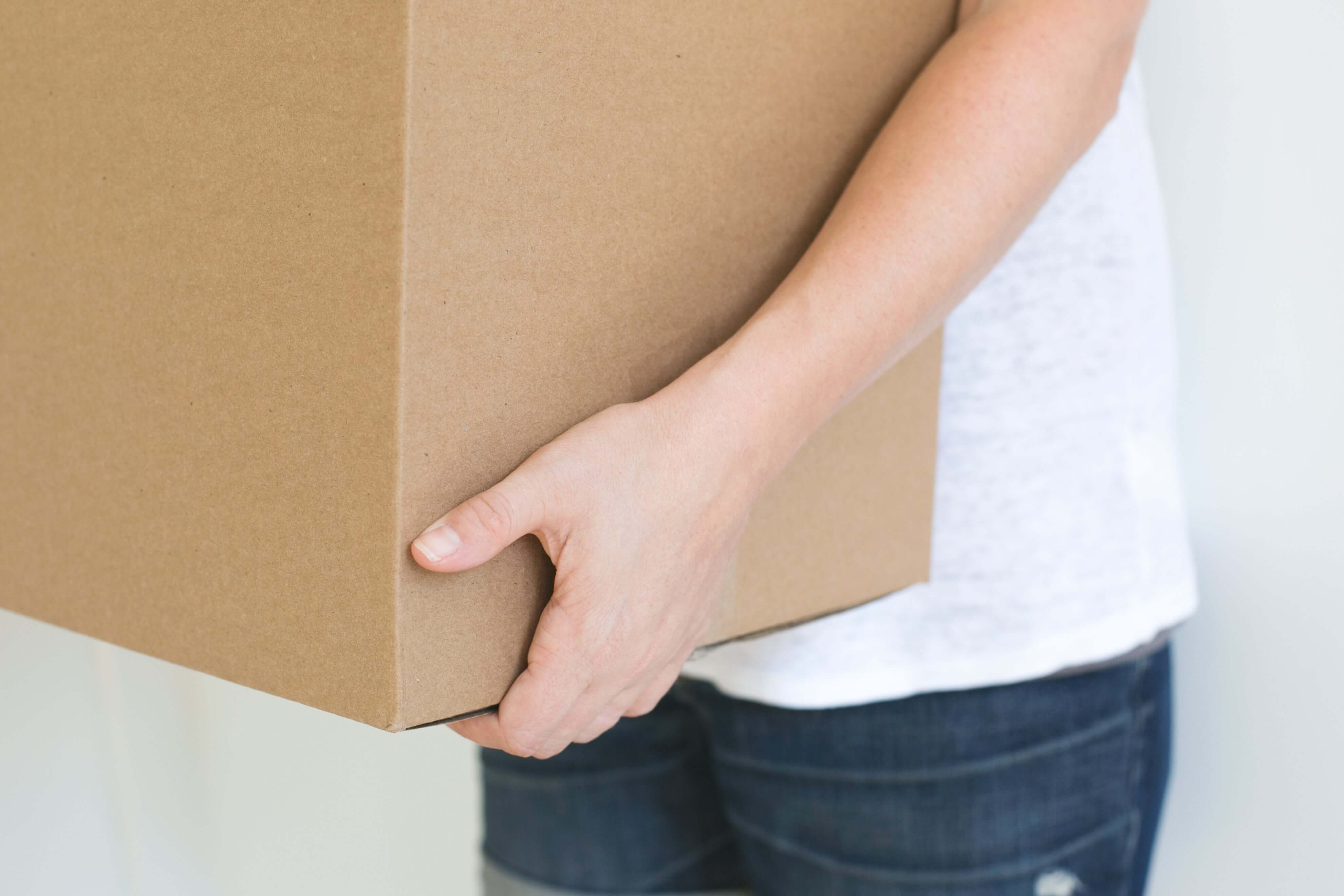 Person holding a cardboard box with a plain background